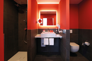  In den Badezimmern treffen rote Wände und schwarze Fliesen auf die eleganten Waschtische und Duschflächen der Kaldewei „Cono“ Serie aus Stahl-Email in Alpinweiß. 